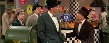 Movie still from “Guys and Dolls” (1955), directed by Joseph L. Mankiewicz – A man in a suit and hat standing in front of a fruit stand; Medium shot, Over the shoulder angle