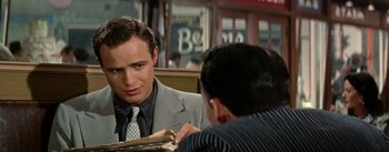 Movie still from “Guys and Dolls” (1955), directed by Joseph L. Mankiewicz – A man sitting at a table in a suit and tie; Close Up shot, Over the shoulder angle