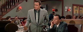 Movie still from “Guys and Dolls” (1955), directed by Joseph L. Mankiewicz – A man in a suit and tie talking on the phone; Medium shot, Over the shoulder angle