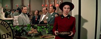 Movie still from “Guys and Dolls” (1955), directed by Joseph L. Mankiewicz – A group of men and women standing around a table with food on it; Medium shot, Over the shoulder angle