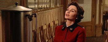 Movie still from “Guys and Dolls” (1955), directed by Joseph L. Mankiewicz – A woman in a red coat standing in front of a row of curtains; Close Up shot, Low angle
