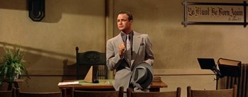 Movie still from “Guys and Dolls” (1955), directed by Joseph L. Mankiewicz – A man in a suit and tie standing in front of a table; Medium shot, Low angle
