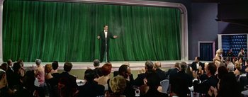 Movie still from “Guys and Dolls” (1955), directed by Joseph L. Mankiewicz – A man standing on a stage in front of an audience; Wide shot, Low angle