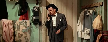 Movie still from “Guys and Dolls” (1955), directed by Joseph L. Mankiewicz – A man wearing a suit and hat talking on a phone; Medium shot, High angle