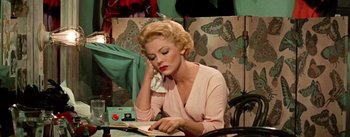 Movie still from “Guys and Dolls” (1955), directed by Joseph L. Mankiewicz – A woman sitting at a table reading a book; Medium shot, High angle