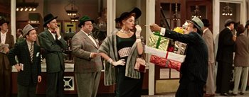 Movie still from “Guys and Dolls” (1955), directed by Joseph L. Mankiewicz – A man is smoking a cigarette next to a woman in a dress; Medium shot, Over the shoulder angle