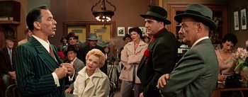 Movie still from “Guys and Dolls” (1955), directed by Joseph L. Mankiewicz – A man and a woman are standing next to each other in front of a crowd; Medium shot, Over the shoulder angle
