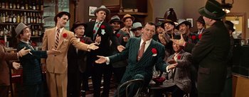 Movie still from “Guys and Dolls” (1955), directed by Joseph L. Mankiewicz – A group of men standing around a man in a green suit; Wide shot, High angle