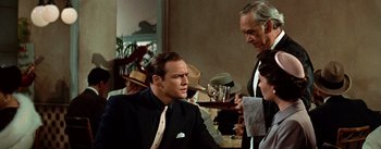 Movie still from “Guys and Dolls” (1955), directed by Joseph L. Mankiewicz – A man in a suit and tie talking to two other men; Medium shot, Over the shoulder angle