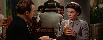 Movie still from “Guys and Dolls” (1955), directed by Joseph L. Mankiewicz – A woman is holding a drink in her hand while standing next to a man in a suit; Close Up shot, Over the shoulder angle