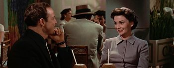 Movie still from “Guys and Dolls” (1955), directed by Joseph L. Mankiewicz – A man and a woman sitting at a table in front of a woman; Medium shot, Over the shoulder angle