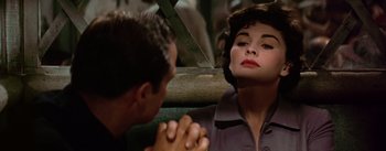 Movie still from “Guys and Dolls” (1955), directed by Joseph L. Mankiewicz – A man and a woman sitting next to each other in front of a wooden fence; Close Up shot, Over the shoulder angle