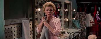 Movie still from “Guys and Dolls” (1955), directed by Joseph L. Mankiewicz – A woman in a pink dress holding onto a towel; Medium shot, Over the shoulder angle