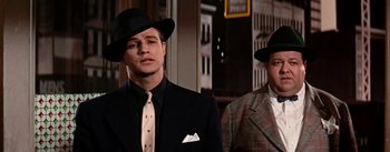 Movie still from “Guys and Dolls” (1955), directed by Joseph L. Mankiewicz – A man in a suit and a man in a hat; Medium shot, Low angle