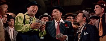 Movie still from “Guys and Dolls” (1955), directed by Joseph L. Mankiewicz – A group of men standing next to each other holding money; Medium shot, Low angle