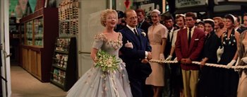 Movie still from “Guys and Dolls” (1955), directed by Joseph L. Mankiewicz – An older woman in a wedding dress and a man in a suit and tie; Medium shot, Over the shoulder angle