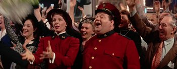 Movie still from “Guys and Dolls” (1955), directed by Joseph L. Mankiewicz – A group of men and women in red uniforms singing together; Medium shot, Low angle