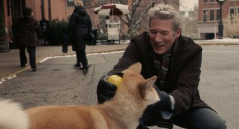Movie still from “Hachi: A Dog's Tale” (2009), directed by Lasse Hallström – An older man playing with a cat on the street; Medium shot, Over the shoulder angle
