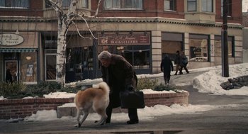 Movie still from “Hachi: A Dog's Tale” (2009), directed by Lasse Hallström – An older woman walking a dog down a sidewalk; Wide shot, Over the shoulder angle