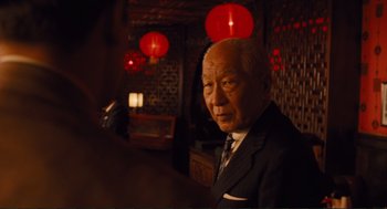 Movie still from “Hail, Caesar!” (2016), directed by Ethan Coen – An older man in a suit and tie in front of red lanterns; Close Up shot, Over the shoulder angle