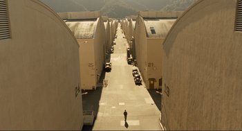 Movie still from “Hail, Caesar!” (2016), directed by Ethan Coen – A person walking down a street near a parking lot; Extreme Wide shot, High angle