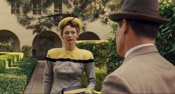 Movie still from “Hail, Caesar!” (2016), directed by Ethan Coen – An older woman wearing a yellow and black hat; Medium shot, Over the shoulder angle