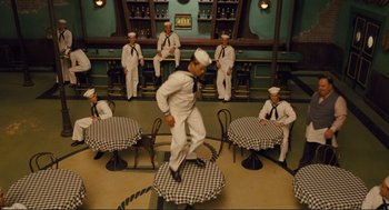 Movie still from “Hail, Caesar!” (2016), directed by Ethan Coen – A man in a sailor's uniform jumping over a table; Wide shot, High angle