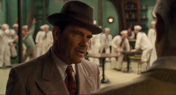 Movie still from “Hail, Caesar!” (2016), directed by Ethan Coen – A man wearing a suit and hat in a room; Medium shot, Over the shoulder angle