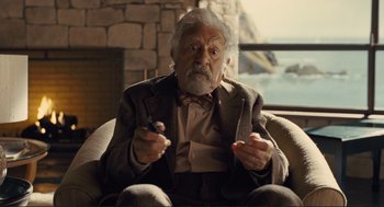 Movie still from “Hail, Caesar!” (2016), directed by Ethan Coen – An older man sitting in a chair holding a cigarette in his hand; Medium shot, Over the shoulder angle