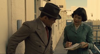 Movie still from “Hail, Caesar!” (2016), directed by Ethan Coen – A man in a suit and a hat standing next to a woman in a green coat; Medium shot, Over the shoulder angle