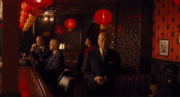 Movie still from “Hail, Caesar!” (2016), directed by Ethan Coen – A group of people sitting in a room with red lanterns; Wide shot, Low angle