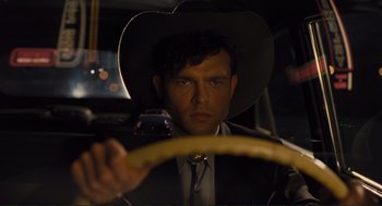 Movie still from “Hail, Caesar!” (2016), directed by Ethan Coen – A man wearing a cowboy hat driving a car at night; Close Up shot, Over the shoulder angle