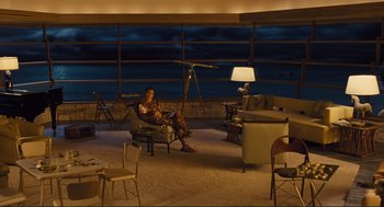 Movie still from “Hail, Caesar!” (2016), directed by Ethan Coen – A woman sitting in a chair in a room with a large window; Wide shot, High angle