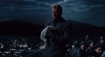 Movie still from “Hail, Caesar!” (2016), directed by Ethan Coen – A man holding a dog while standing in front of a body of water at night; Medium shot, Low angle