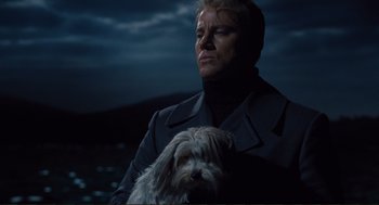 Movie still from “Hail, Caesar!” (2016), directed by Ethan Coen – A man holding a dog while standing in front of a body of water at night; Medium shot, Low angle