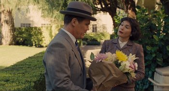 Movie still from “Hail, Caesar!” (2016), directed by Ethan Coen – A man in a suit and a woman in a hat holding flowers; Medium shot, Over the shoulder angle