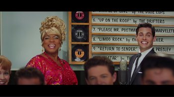 Movie still from “Hairspray” (2007), directed by Adam Shankman – A woman in a red dress and a man in a black suit and a microphone; Medium shot, Low angle