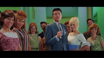 Movie still from “Hairspray” (2007), directed by Adam Shankman – A group of people standing in a room with a man in a blue suit; Medium shot, Low angle