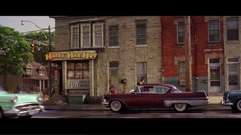 Movie still from “Hairspray” (2007), directed by Adam Shankman – An old car is parked in front of a building; Wide shot, Low angle