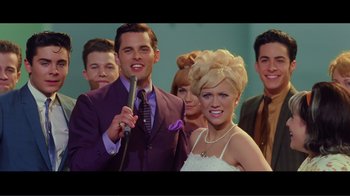 Movie still from “Hairspray” (2007), directed by Adam Shankman – A man and woman posing for a picture with other people; Medium shot, Low angle