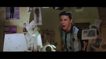 Movie still from “Hairspray” (2007), directed by Adam Shankman – A man standing in front of a bunch of pictures; Medium shot, High angle