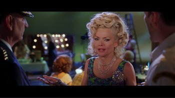 Movie still from “Hairspray” (2007), directed by Adam Shankman – An older woman with blonde curly hair wearing a necklace; Medium shot, Over the shoulder angle