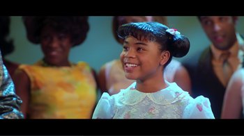 Movie still from “Hairspray” (2007), directed by Adam Shankman – A young girl smiles brightly while standing in front of a group of women; Close Up shot, Over the shoulder angle