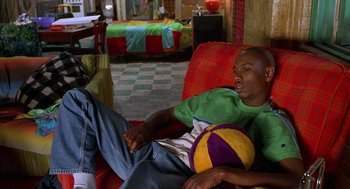 Movie still from “Half Baked” (1998), directed by Tamra Davis – A man sitting on a red couch holding a ball; Medium shot, High angle