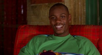 Movie still from “Half Baked” (1998), directed by Tamra Davis – A man sitting on a red couch smiling for the camera; Close Up shot, High angle