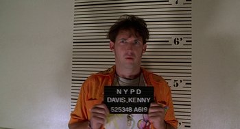 Movie still from “Half Baked” (1998), directed by Tamra Davis – A man holding up a mug shot in front of a police wall; Close Up shot, Low angle