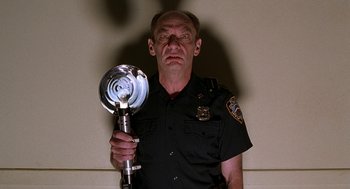 Movie still from “Half Baked” (1998), directed by Tamra Davis – A man in a police uniform holding a fire hydrant; Close Up shot, Low angle