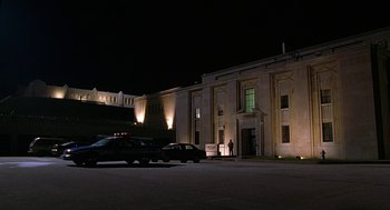 Movie still from “Half Baked” (1998), directed by Tamra Davis – A police car parked in front of a large building at night; Extreme Wide shot, Low angle