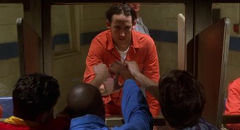 Movie still from “Half Baked” (1998), directed by Tamra Davis – A group of people in a room with a man in an orange shirt; Medium shot, Over the shoulder angle