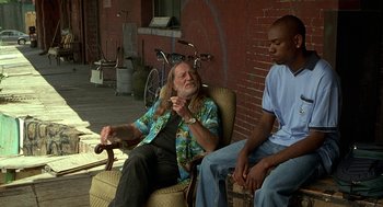 Movie still from “Half Baked” (1998), directed by Tamra Davis – A man sitting in a chair next to a man sitting on a bicycle; Medium shot, Low angle